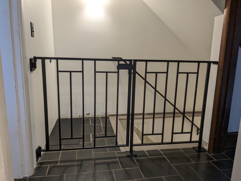 Custom flat bar steel safety gate with geometric vertical baluster design, powder coated black