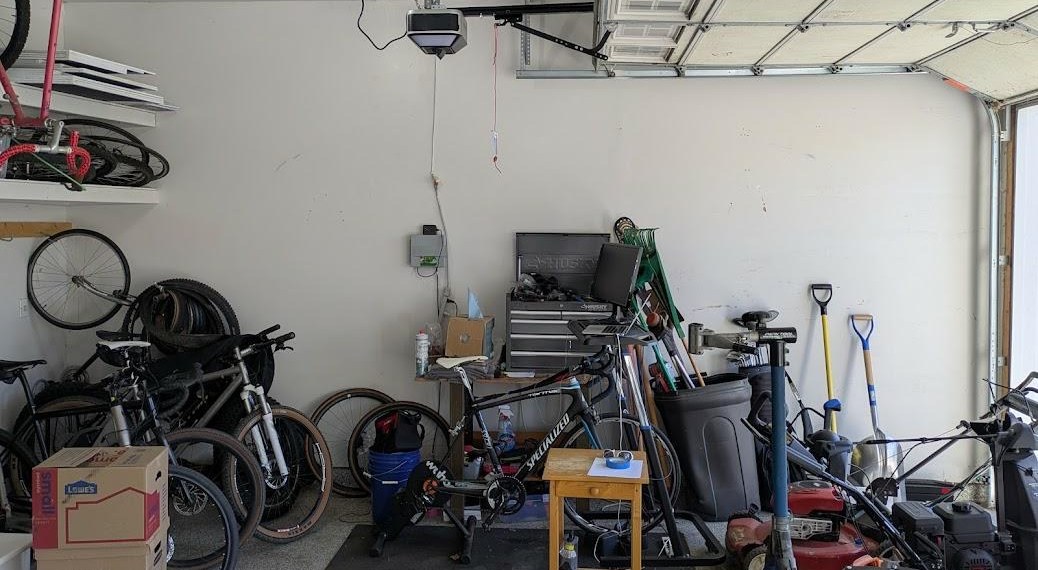 Garage corner before the redesign, with bikes leaning in a pile, a mower in the way and a blank back wall